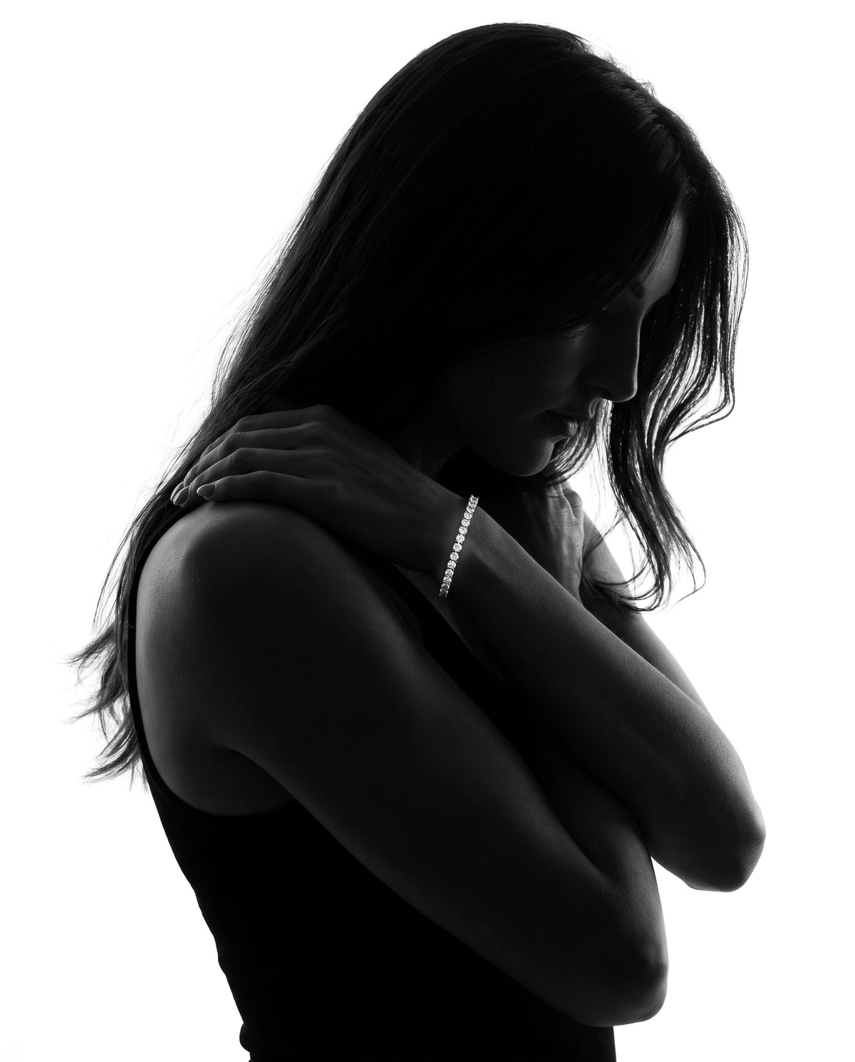 Silhouette of a woman with her arms wrapped around herself, wearing a 2mm lab-grown moissanite tennis bracelet