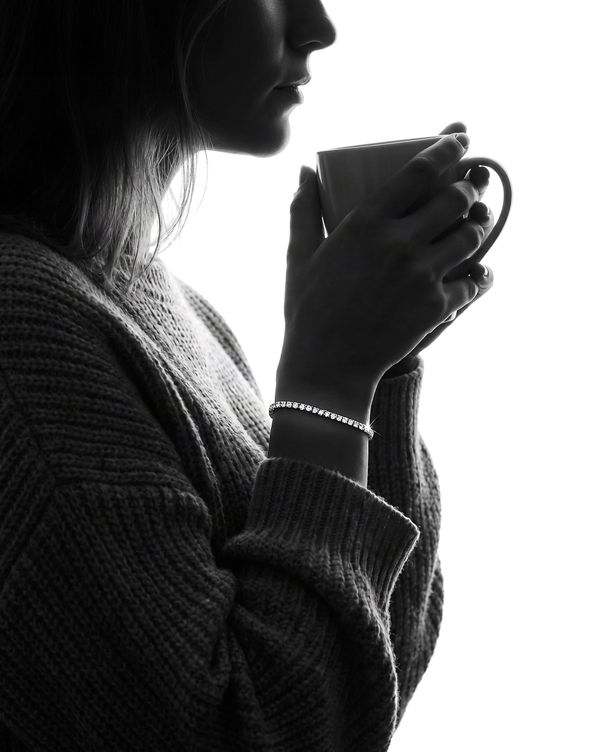 Woman in a knit sweater holding a coffee mug, wearing a 2mm lab-grown moissanite tennis bracelet